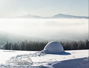 Real snow igloo house in the winter Carpathian mountains. Snow-covered firs and mountain peaks in fog on the background