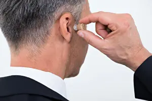 Hear Prints: Rear view of businessman inserting hearing aid in ear over white background