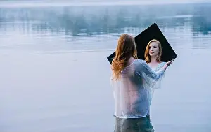 Emerging Prints: Rear view of young woman standing in lake holding mirror looking at reflection