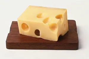 Food Preparation Prints: Rectangular block of cheese with holes on wooden board, close up