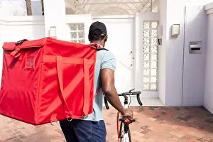 Parcel Prints: Red insulated delivery bag is dominating frame while bicycle is being pushed at house entrance