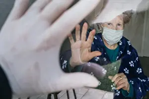 Relative Prints: Redhead aged female in medical mask waving hand through window to relative while isolating at home