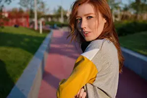 Redhead Prints: Redhead girl with freckles and green eyes with headphones on her neck stands on the street in a half turn