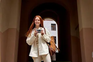 Redhead Prints: redhead Woman tourist walking on street in european old city using camera