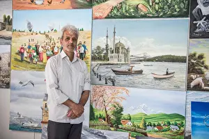 Refugee Camp Prints: A refugee man poses in front of the paintings he has painted in the painting classes he attends in the Kilis refugee