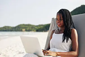 Surfer Prints: Relaxed beautiful young Black woman resting on beach on sunny day and working on laptop