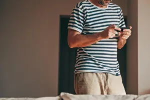 Texting Prints: Relaxed middle-aged man in striped t-shirt and beige shorts stands casually
