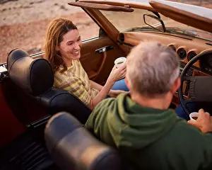 Rising Prints: Retired Senior Couple In Classic Sports Car With Hot Drink At Beach Watching Sunrise