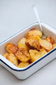 Wholesome Prints: Roast potatoes in an white enamel roasting dish on a white background