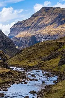 Travel Brochure Prints: A rocky scenic river in Saksun, Faroe Islands with a steep mountain on the background