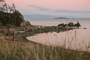 Coastal View Prints: Rocky shoreline with driftwood at sunset, calm water and islands