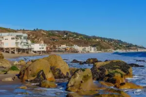 Crashing Prints: Rocky shoreline of Malibu Beach with cascading waves and coastal homes perched on the hillside