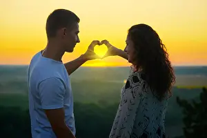 Nightfall Prints: romantic couple at sunset make a heart shape from hands