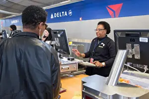Airlines Prints: Romulus, Michigan - A Delta Air Lines ticket agent checks in a passenger at Detroit Metro Airport