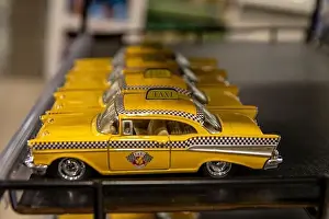 Row of miniature yellow taxi cabs lined up on a shelf - classic New York City Checker Taxi design