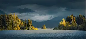 Storm Clouds Prints: Row of sunlit trees in the middle of a beautiful blue lake