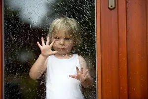 Sad child behind the window on a rainy day