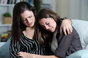 Worry Prints: Two sad friends or sisters crying together on a couch in the living room at home