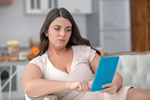 Long Haired Prints: Sad woman looking at a tablet, reclining on a sofa