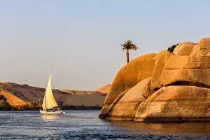 Yachting Prints: Sailboat on the Nile river at sunset, rock with ancient carvings in the front, Egypt