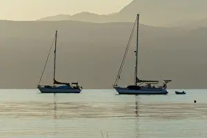 Open Water Prints: Two sailboats anchored on a calm lake at sunset with mountains in the background
