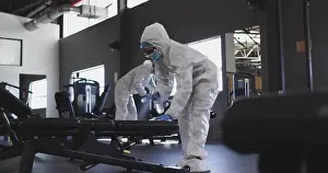 Bending Prints: Sanitation worker in coveralls cleaning weight bench at gym, with spray bottles and cloths
