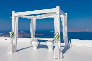 Santorini Island, Greece. Wedding decoration on a popular couple destination. Elegant wedding arch with white flowers, vases on background of blue sea