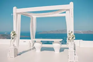 Santorini Island, Greece. Wedding decoration on a popular couple destination. Elegant wedding arch with white flowers, vases on background of blue sea