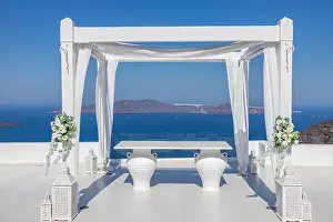 Santorini Island, Greece. Wedding decoration on a popular couple destination. Elegant wedding arch with white flowers, vases on background of blue sea