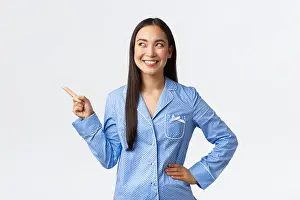 Awake Prints: Satisfied happy asian woman in blue pajamas smiling broadly as pointing and looking at upper left corner