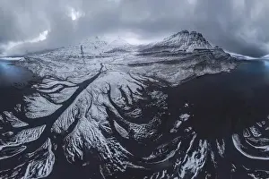 Scenic aerial view of river estuary located in valley near snowy mountain range on cold winter day in southeast Iceland