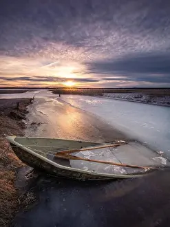 Scenic landscape with sunset and abandoned boat at spring evening in Finland. Boat is almoust in the ice