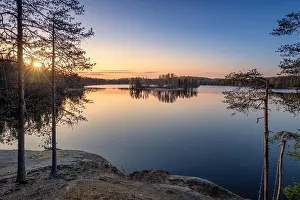 Scenic landscape with sunset, peaceful lake and tree roots at calm spring evening in Finland
