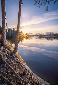 Scenic landscape with sunset, peaceful lake and tree roots at calm spring evening in Finland