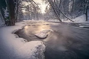 Scenic winter landscape with flowing river and morning light in Finland. Snowy trees