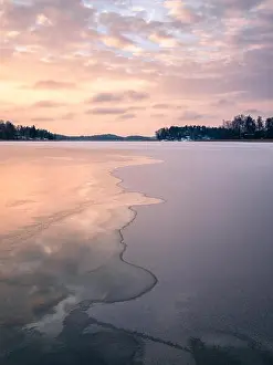 Scenic winter landscape with frozen lake and water at evening sunset in Finland