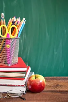 School supplies, apple and books on wooden table in front of the school chalkboard. Back to school concept