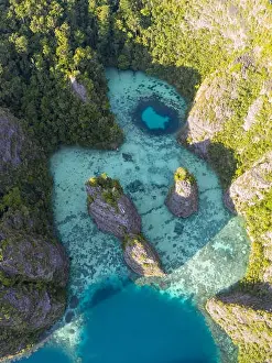 Seen from above, remote islands are surrounded by coral reefs in Raja Ampat, Indonesia. This region is known as the heart of the Coral Triangle