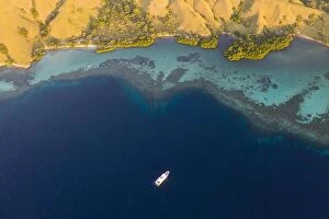 Aerial Landscape Collection: Seen from a bird's eye view, an idyllic island is surrounded by a healthy coral reef in Komodo