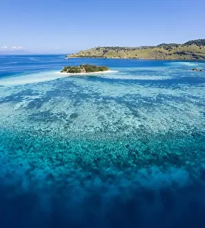 Seen from a bird's eye view, an idyllic tropical island is surrounded by a healthy coral reef in Komodo National Park, Indonesia