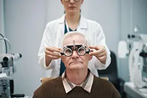 Checkup Prints: Senior Caucasian man sitting while female doctor adjusting phoropter during eye examination in clinic