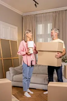 Pensioners Prints: Senior couple moving house packing boxes with belongings together in their home