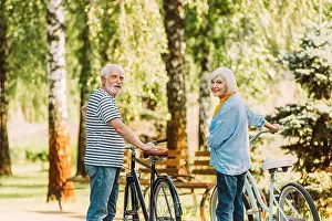Senior couple smiling at camera while standing near bicycles in park
