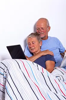 On White Prints: Senior Couple with Tablet and Newspaper in Bed
