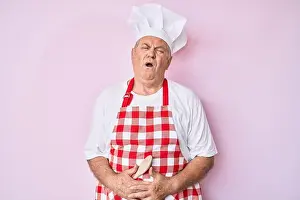 Abdomen Prints: Senior grey-haired man wearing professional baker apron with hand on stomach because nausea