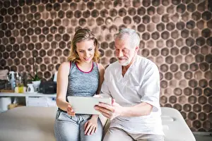 Masseur Prints: Senior male physiotherapist and young woman with tablet sitting