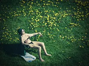 Unrecognizable Prints: Senior woman sunbathes, sitting on a chaise longue in a dandelion field