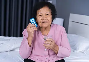 Medicament Prints: senior woman taking pill with glass of water in a bed