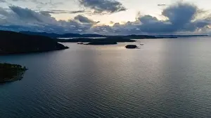 A serene aerial view of a large fjord with small islands and distant hills under a cloudy sky at dusk