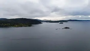 A serene landscape featuring a calm fjord surrounded by forested hills under a cloudy sky